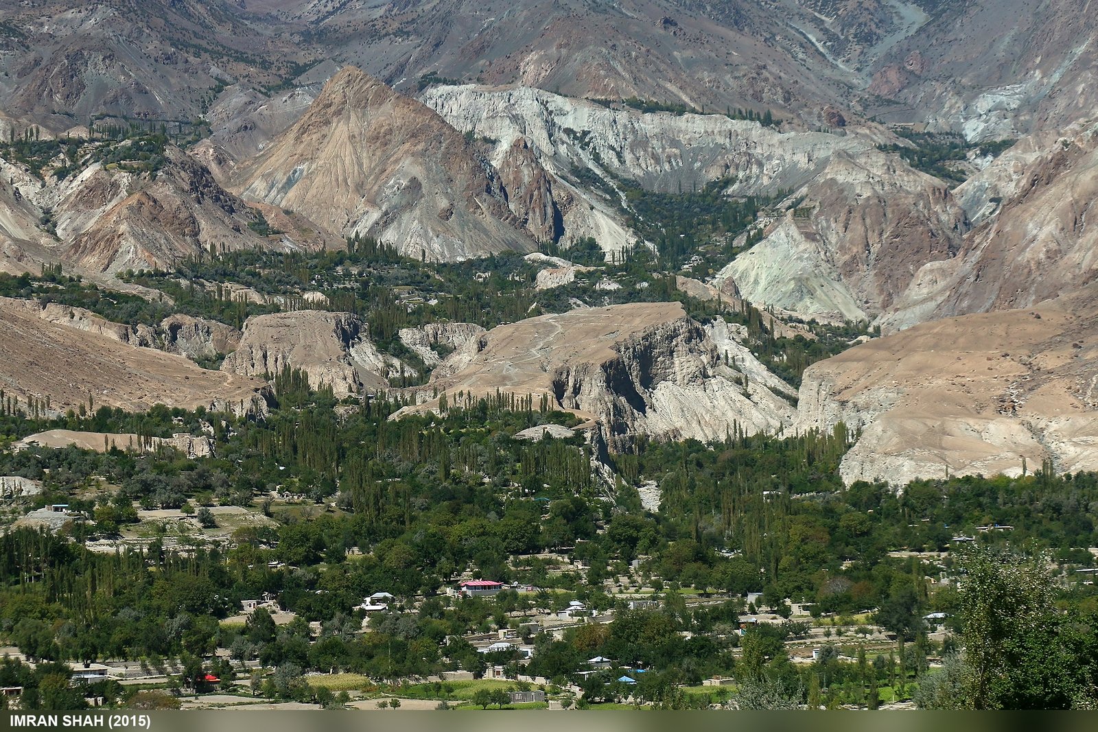 Green valley settlement near Chatorkhand in Ishkoman Valley beneath barren mountains