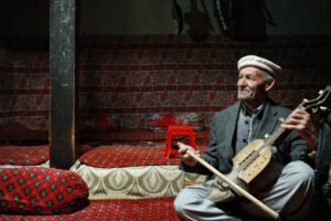 An elderly man in a white cap playing the Ghizek indoors in Ghulkin, Hunza