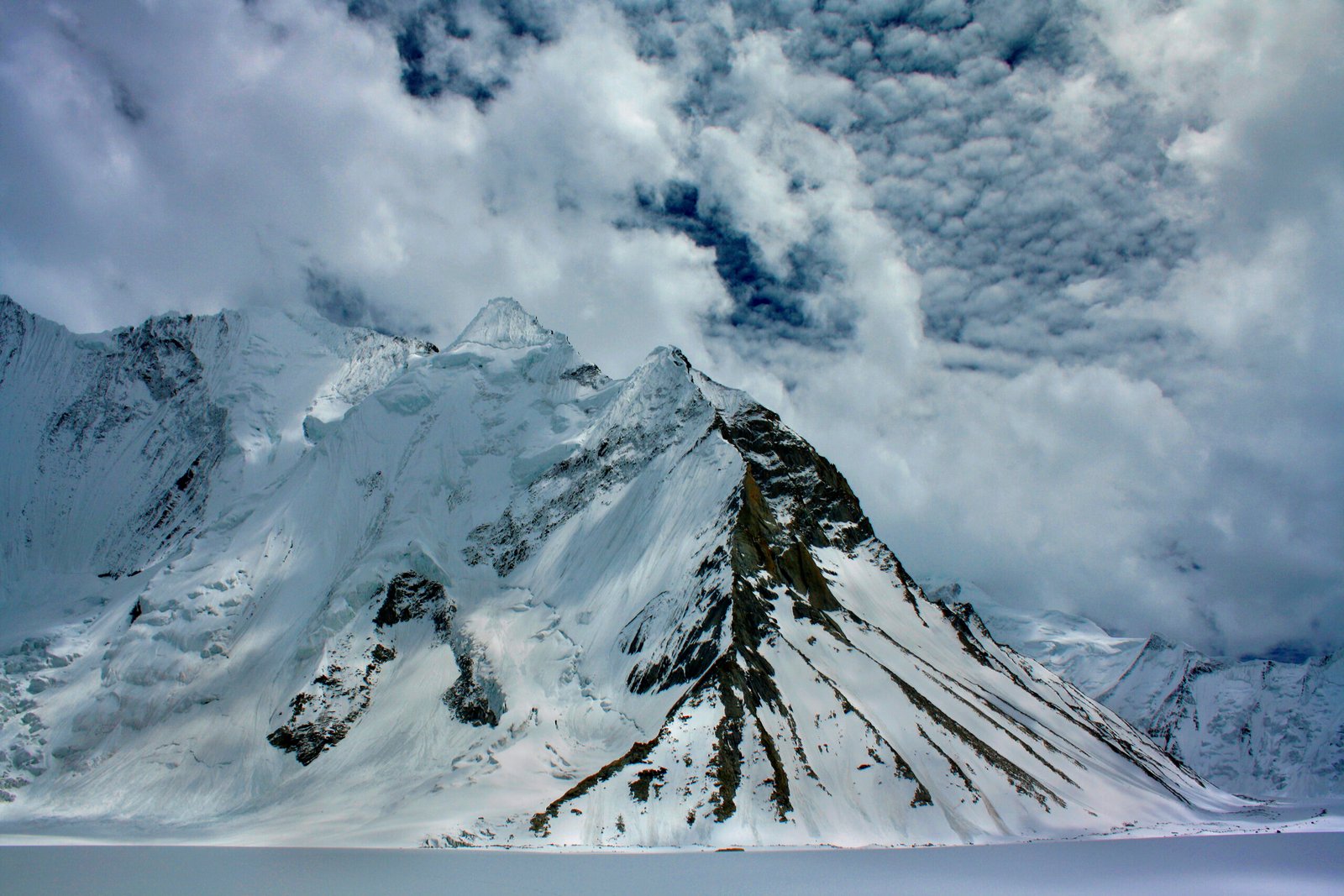 A snowy Karakoram peak under storm clouds near Ali Camp in the K2 region.