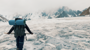 Trekker with a large backpack walking across snow towards snowy peaks near Gondogoro La.