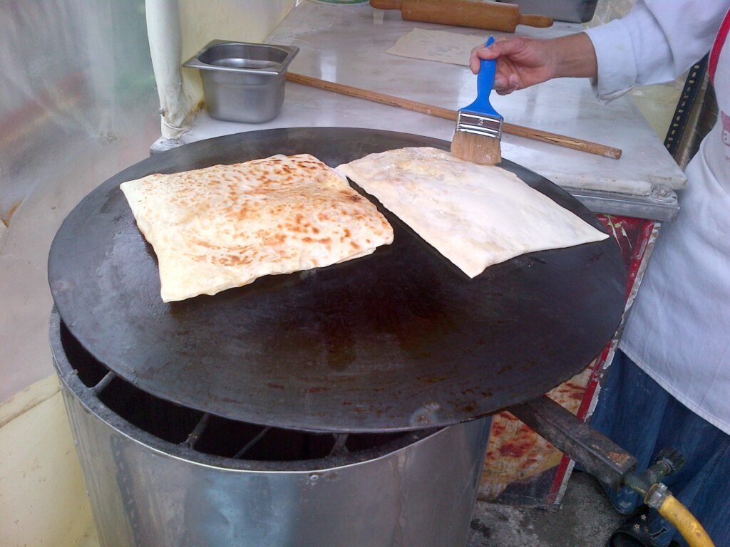 Stuffed flatbread cooking on a large flat griddle