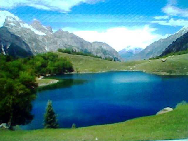 Blue mountain lake with grassy banks and trees in Haramosh Valley
