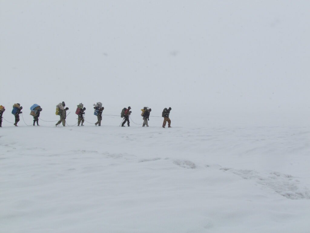 Roped trekkers and porters crossing snow on the Biafo Glacier towards Snow Lake