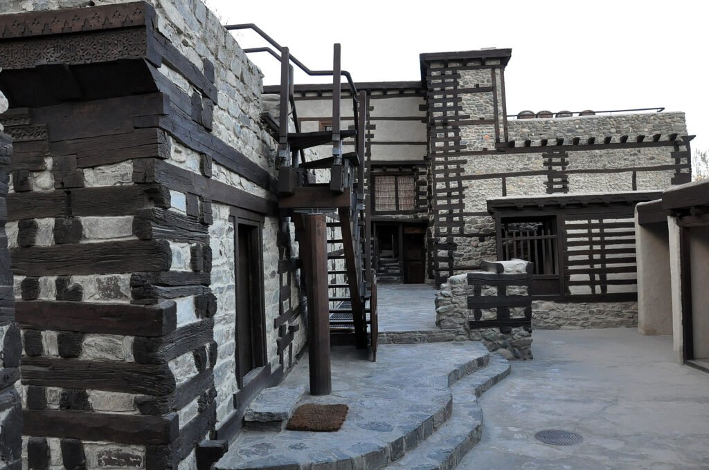 Stone-and-timber courtyard inside Shigar Fort, with a wooden staircase and carved balconies