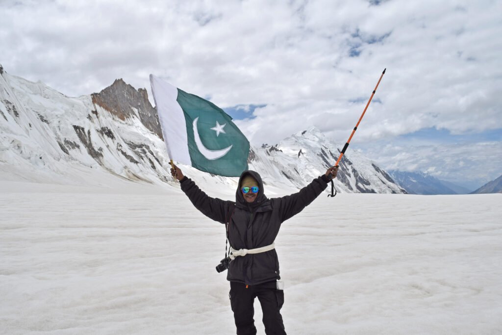 Trekker holding a Pakistan flag on a snowfield at Hispar La with snow-covered peaks behind