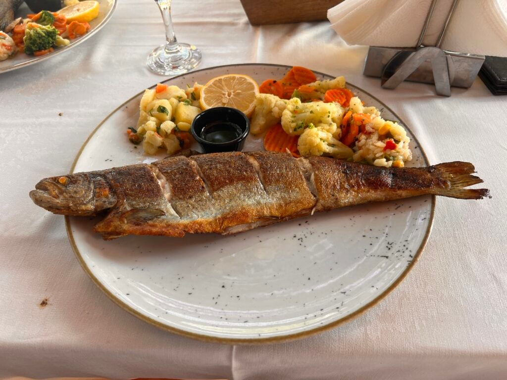 A whole grilled trout served with vegetables and rice