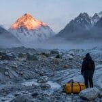 K2 at dawn from Concordia on the Baltoro Glacier with expedition tents and a trekker's duffel bag — K2 base camp trek gear essentials.