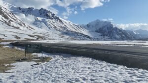 Paved road through snow at Khunjerab Pass, with a national park sign