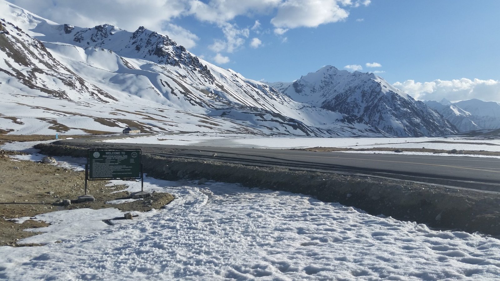 Paved road through snow at Khunjerab Pass, with a national park sign
