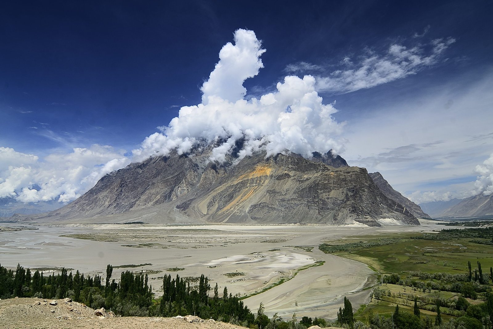Wide braided Shigar River valley with green fields and poplars below barren mountains